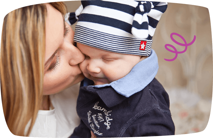 Madre besando tiernamente a su bebé vestido con ropa de rayas, capturando un gesto lleno de amor y afecto.