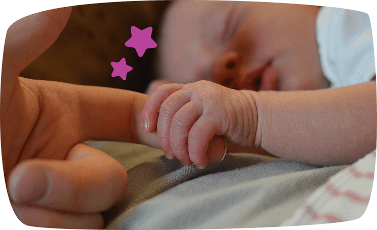 Primer plano de una mano de recién nacido agarrando el dedo de un adulto mientras duerme, creando un momento íntimo y tierno.