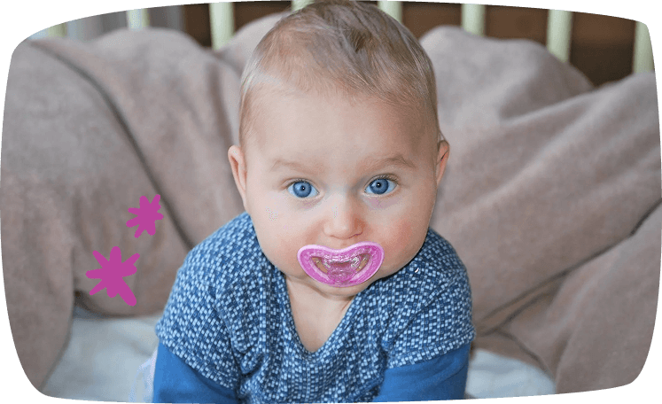 Bebé de ojos azules con chupete azul sonriendo hacia la cámara.