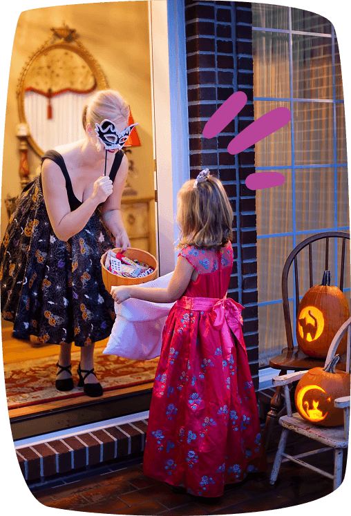 Una mujer disfrazada da caramelos a una niña en Halloween, ilustrando el trabajo de animador infantil durante eventos festivos.