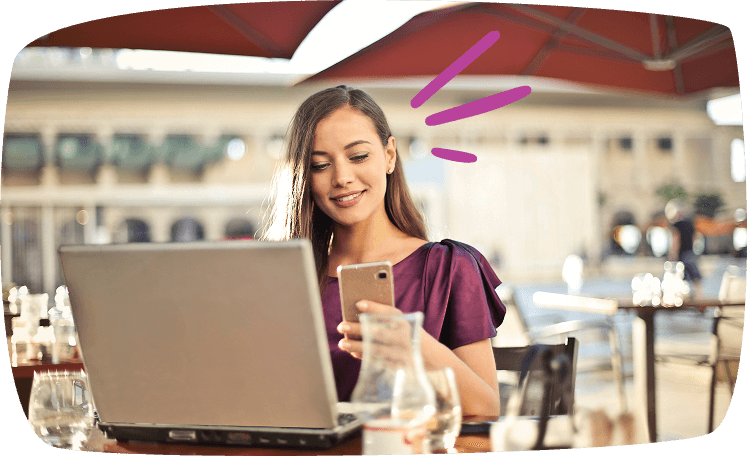 Mujer joven trabajando desde la terraza de un café, usando un portátil y un móvil, representando el teletrabajo para ganar dinero extra.