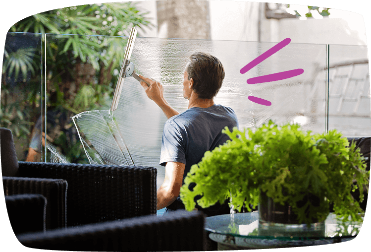 Hombre limpiando un ventanal con escobilla en la terraza de casa, realizando tareas de limpieza de cristales