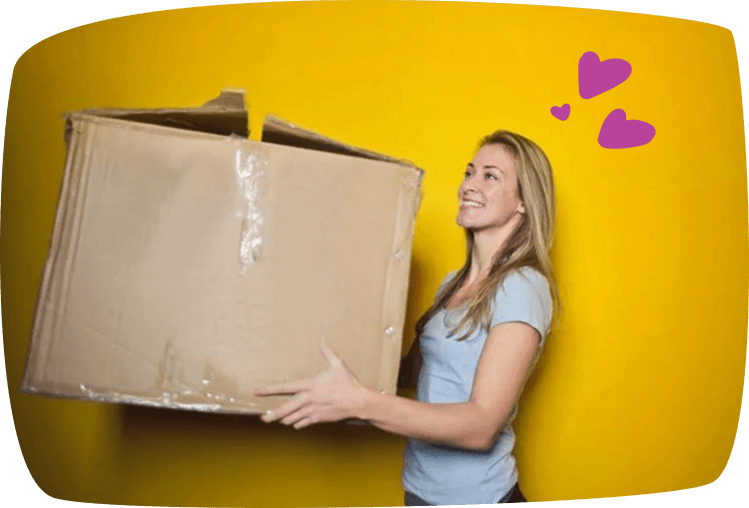 Mujer joven sonriendo mientras sostiene una gran caja de cartón frente a un fondo amarillo, ilustrando el trabajo de mudanzas para ganar dinero extra.