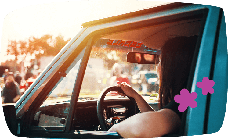 Mujer conduciendo un coche antiguo durante el atardecer, vista lateral desde la ventanilla abierta.