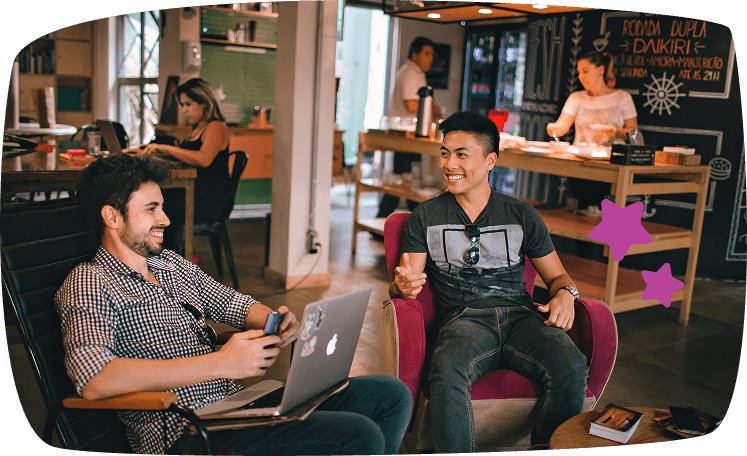 Dos estudiantes conversando y riendo en una cafetería con portátil sobre la mesa, ambiente relajado y colaborativo.