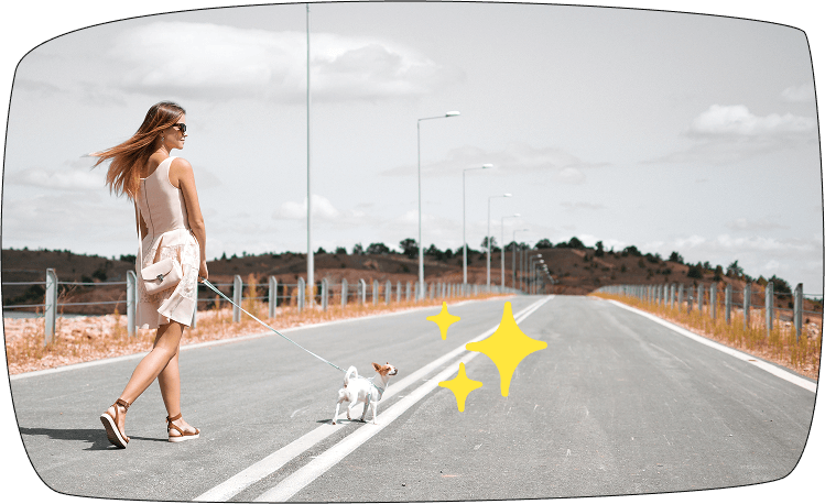 Mujer paseando con su perro por una carretera vacía en un entorno natural, disfrutando del paseo.