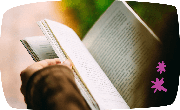 Primer plano de un libro abierto sostenido por una persona mientras lee al aire libre.