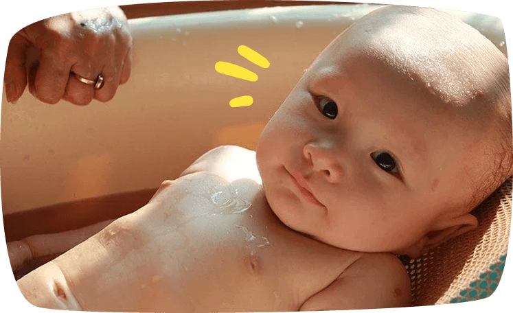 Bebé en la bañera siendo bañado con cuidado por un adulto.