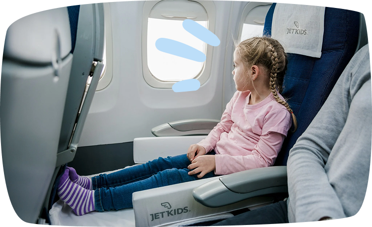 Niña sentada cómodamente en un avión con los pies extendidos sobre una JetKids BedBox