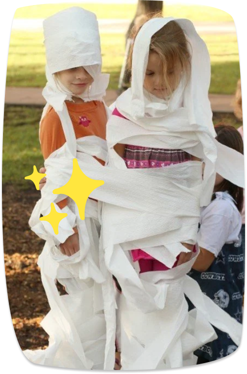 Dos niñas envueltas en papel higiénico jugando a crear disfraces de momias en una actividad de Halloween.