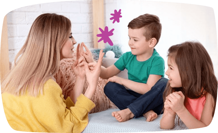 Mujer enseñando a contar con los dedos a dos niños pequeños en una habitación, todos sonriendo.