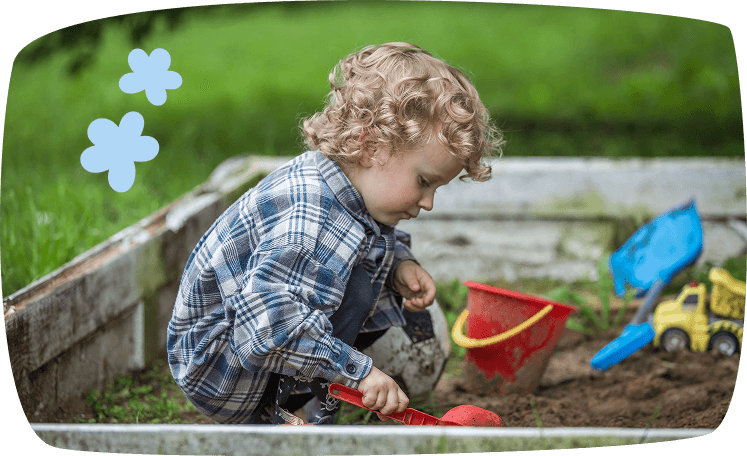 Niño jugando en el arenero con pala y cubo, disfrutando de actividades sensoriales y de exploración al aire libre.