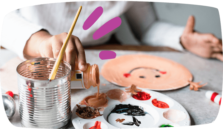 Niño pintando un plato de papel con pinceles y colores acrílicos, participando en una manualidad creativa.