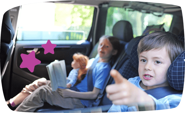 Niños viajando en coche, uno de ellos señalando hacia fuera con entusiasmo mientras otro lee un libro en el asiento trasero.