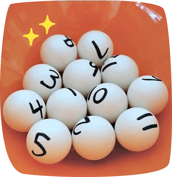 Pelotas de ping pong numeradas del 1 al 12 en un cuenco naranja, para un juego de coordinación y aprendizaje de números.