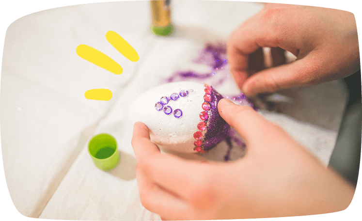 "Huevos de Pascua pintados a mano con puntos y rayas de colores, colocados en una bandeja de plástico transparente."