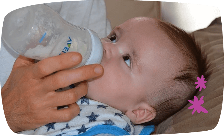 Bebé recostado tomando biberón de manos de un adulto.