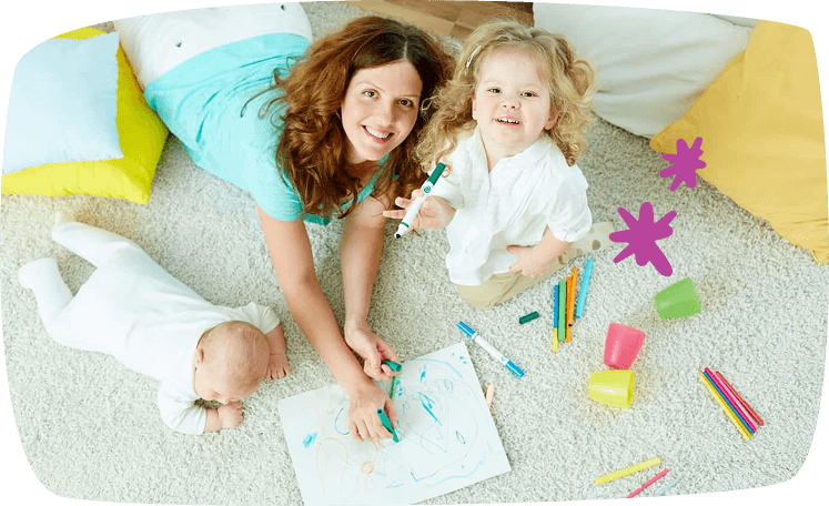 Niñera o madre jugando en el suelo con dos niños pequeños y material de dibujo.