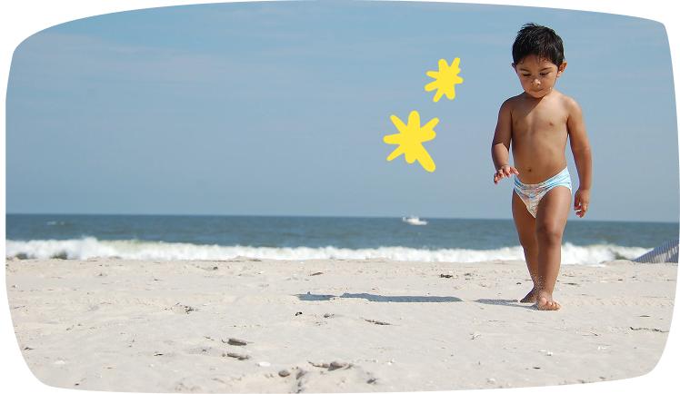 Niño pequeño caminando por la playa con pañal durante el verano.