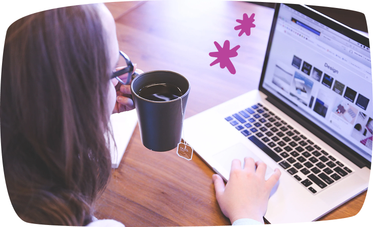 Mujer sosteniendo una taza de té mientras navega en su computadora portátil.