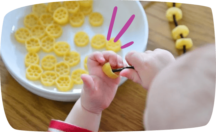 Niño realizando un collar de pasta como actividad Montessori de motricidad fina