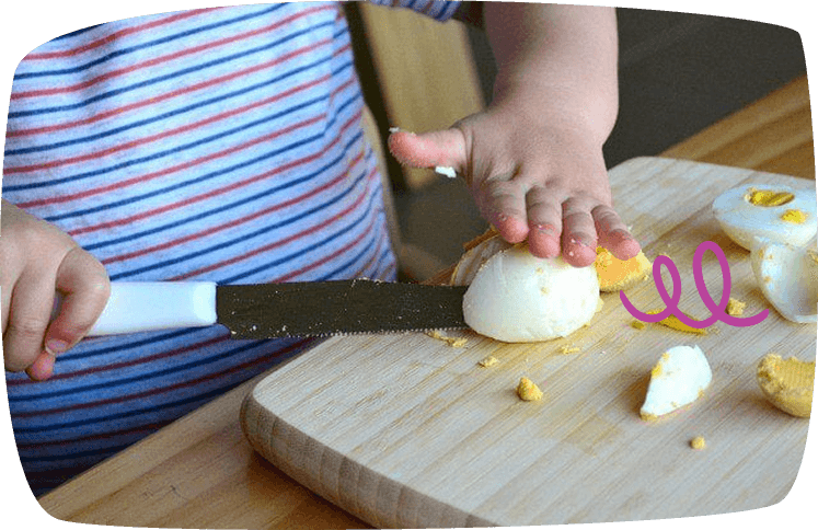 Niño cortando un huevo cocido con cuchillo en actividad Montessori de vida práctica