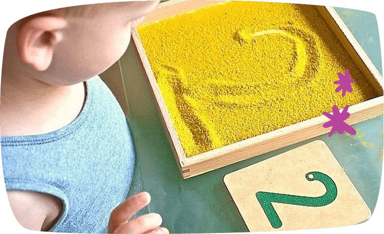 Niño escribiendo números con el dedo en una pizarra de arena Montessori