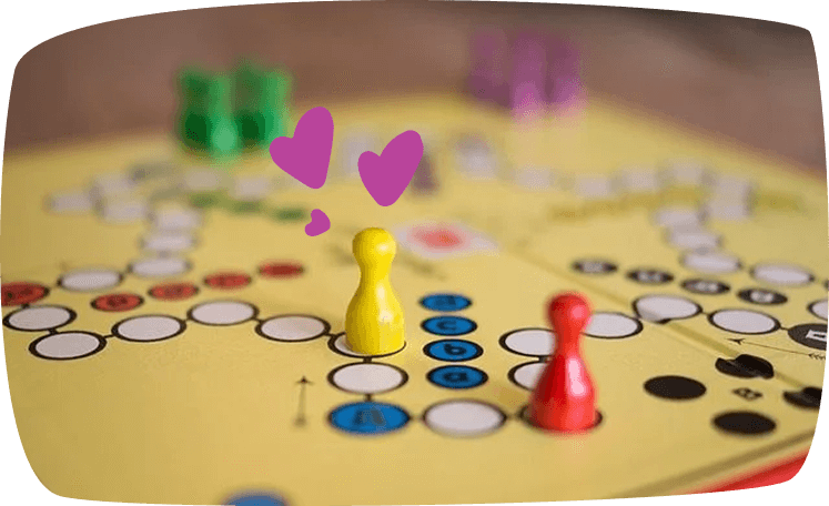 Primer plano de un juego de mesa clásico con fichas de colores, destacando una ficha amarilla en el centro, decorado con corazones morados.