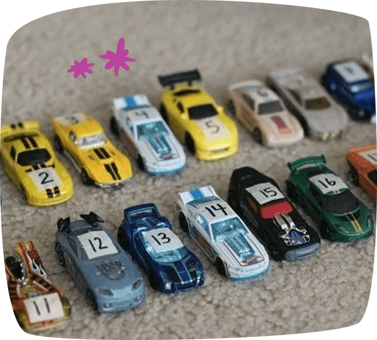 Coches de juguete con pegatinas numeradas alineados en el suelo, como parte de un juego de reconocimiento de números.