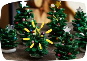 Adornos de Navidad con forma de árbol hechos con piñas pintadas de verde y decoradas con estrellas y bolas de colores.