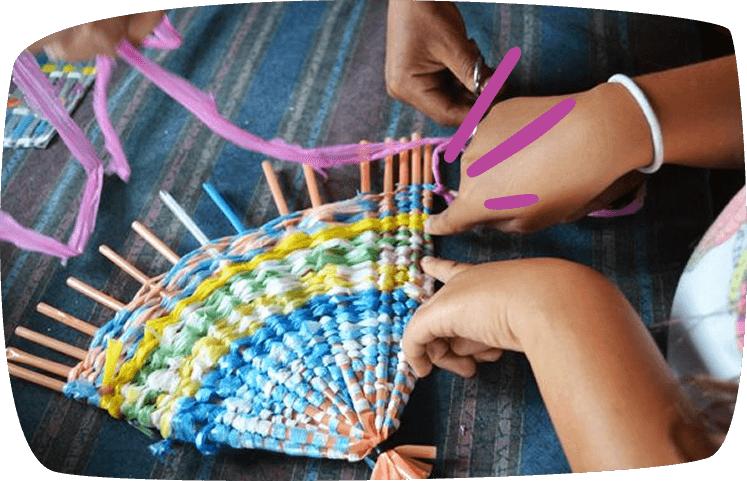 Manos infantiles tejiendo un abanico con pajitas de colores y tiras plásticas, desarrollando la motricidad.