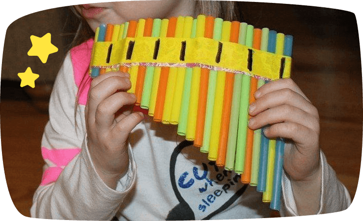 Niña tocando una flauta de pan hecha con pajitas de colores pegadas con cinta decorativa.