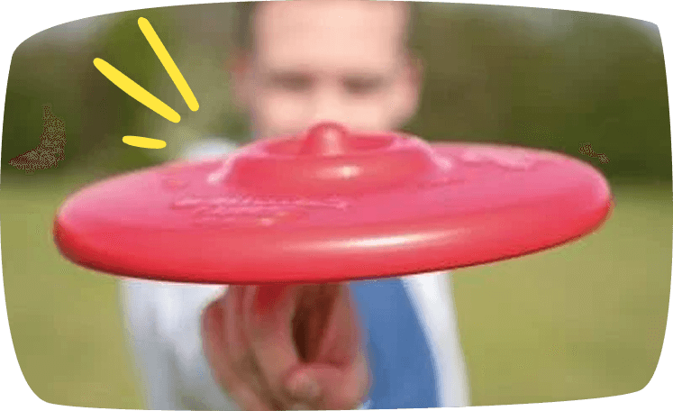 Niño lanzando un frisbee rojo al aire en un parque al aire libre, disfrutando de un juego al exterior.