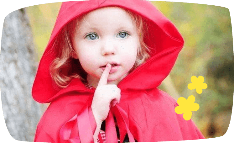 Niña disfrazada de Caperucita Roja con capa roja, llevándose un dedo a los labios en señal de silencio.